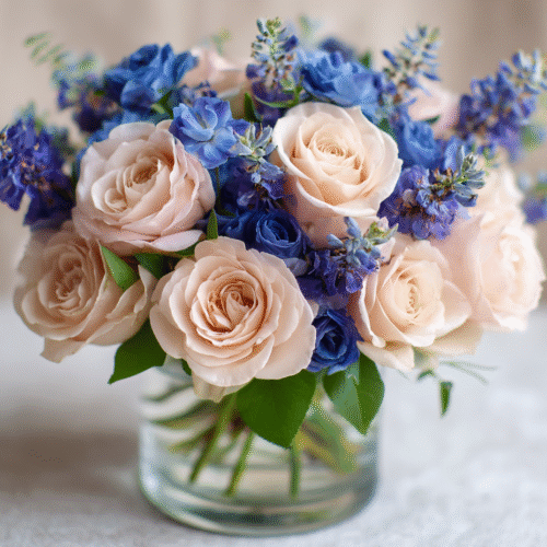 roses and blue rununculus and dark blue delphinium arrangement in clear pot